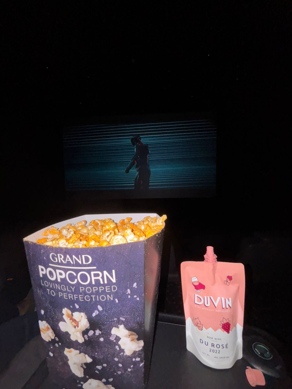 Popcorn bucket and 'Duvin' bottle on a dark surface with a screen in the background